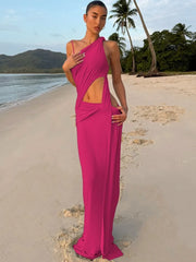 Woman in a bright pink dress standing on a beach with palm trees and mountains in the background.