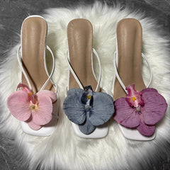 Three pairs of sandals with floral decorations on a fluffy white surface.
