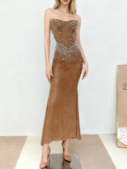 A model wearing a strapless embellished mermaid dress standing in a studio with smooth posture and elongated ankle-length drape.