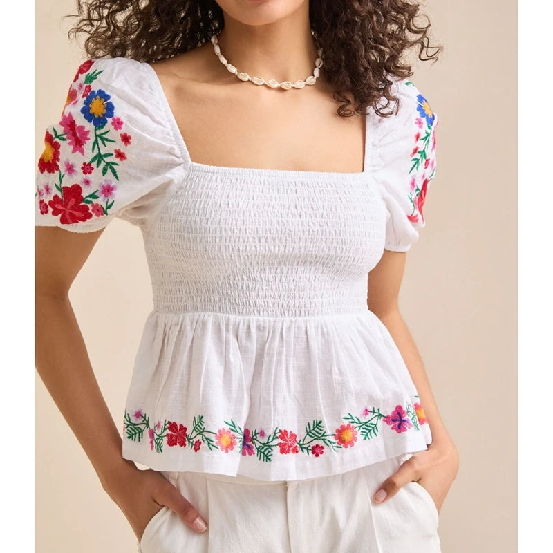 Woman wearing a white embroidered blouse with puff sleeves and peplum hem on a beige background