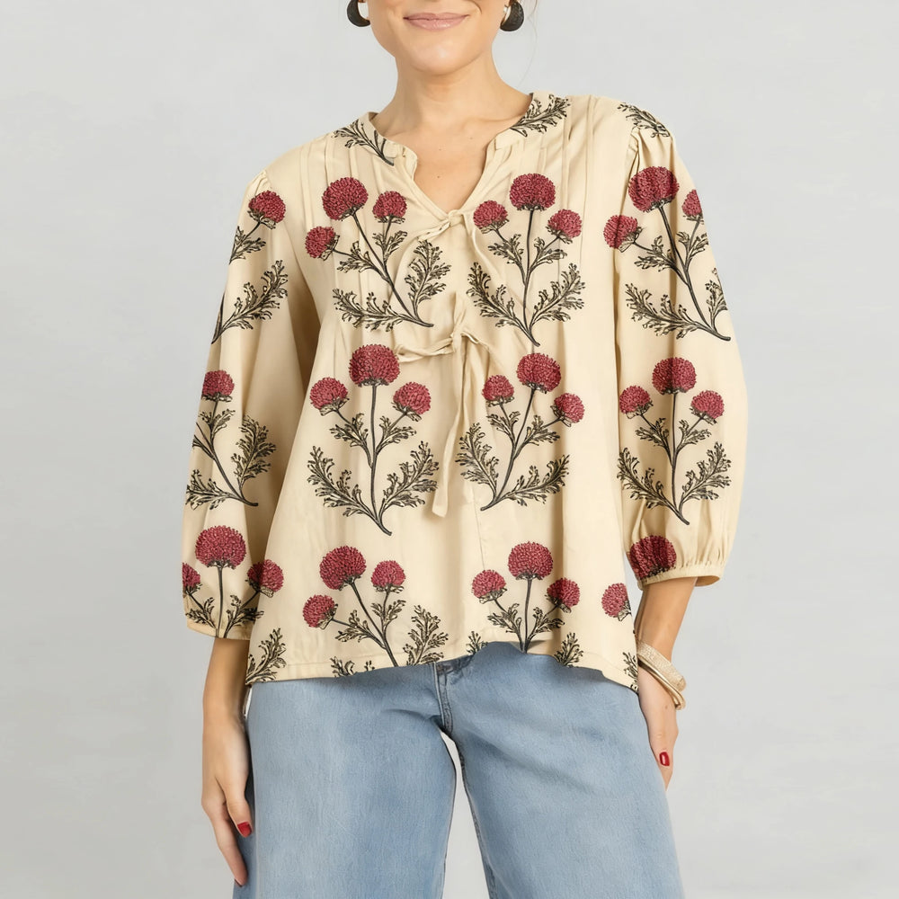 Model wearing a beige embroidered tie-neck blouse styled with denim, standing against a neutral studio background.