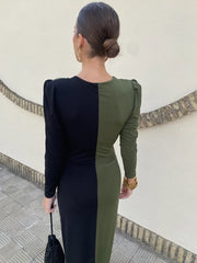 Woman wearing a black and green dress with a white wall and decorative elements in the background