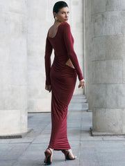 Woman in a figure-flattering cutout maxi dress in rich red for upscale night settings, standing in an architectural setting.