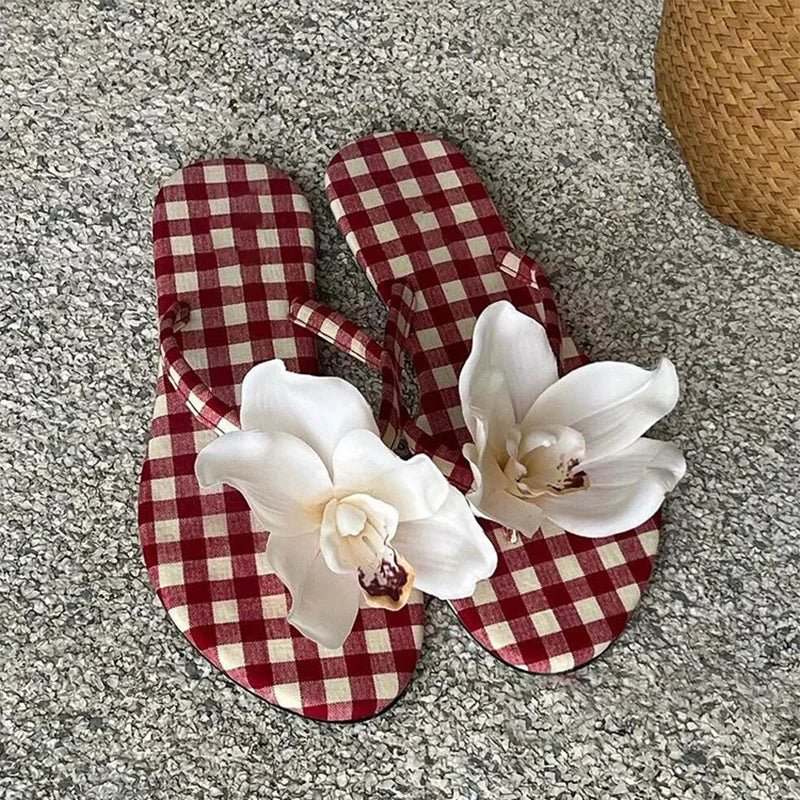 Red and white checkered flip-flops with white flowers on a gray surface