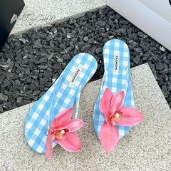 Flat thong summer sandals for women with a lily flower design, Blue checkered flip-flops with pink flowers on a textured surface