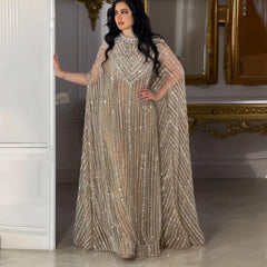 Woman in a floor-length tulle embellished cape dress with radiant crystal details standing in a room with decorative elements.