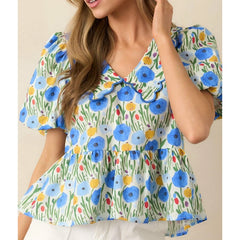 Woman wearing a floral puff sleeve babydoll blouse styled with white pants against a beige background