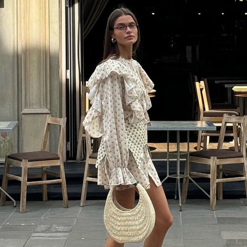Woman in a polka dot dress, ruffled shoulder, and floral fabric texture on mini shirt dress, holding a straw bag in an outdoor cafe setting.