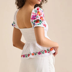 Woman wearing a smocked summer top with colourful floral details  on a beige background