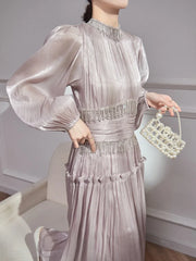 Full look showing the pleated skirt in motion with a structured high neck and long sleeves, styled for an elegant occasion.