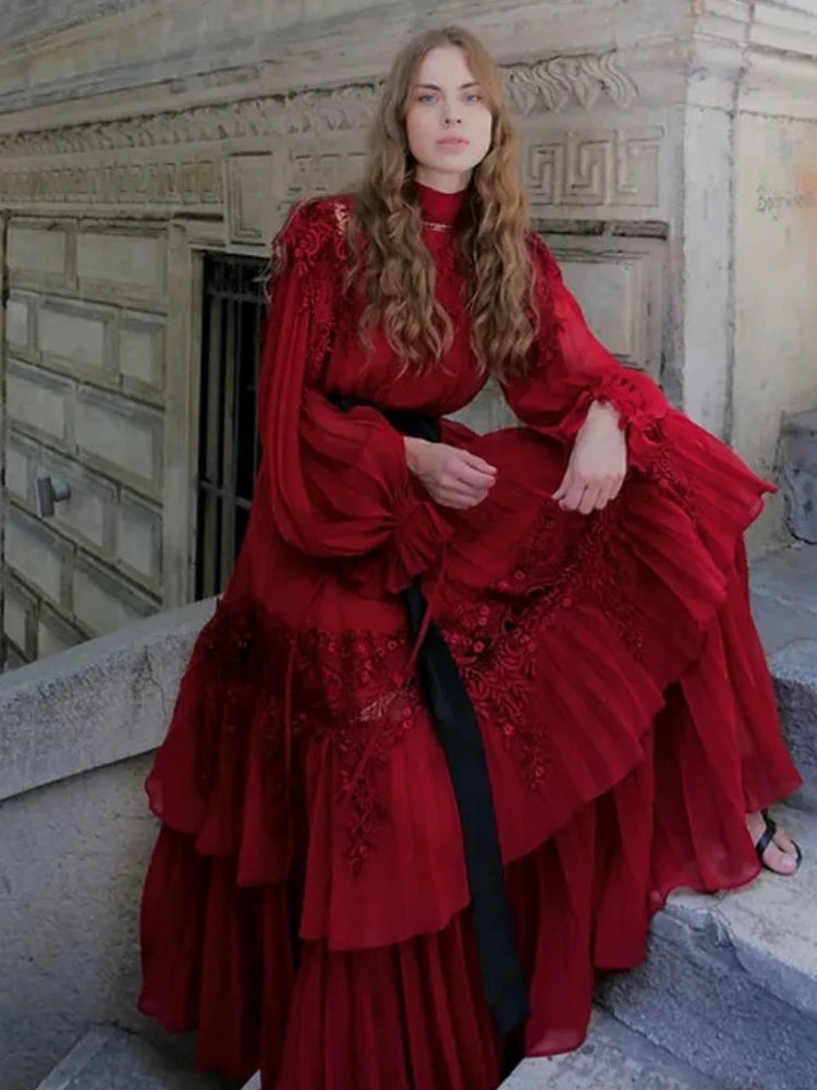 Woman in a flowing red gown styled for gala and evening events sitting on steps with classical architecture in the background