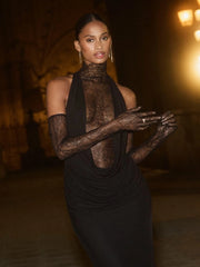 Woman in a folds detail empire waist evening dress in black with lace accents against a dark background