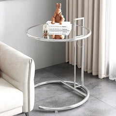 Round glass side table with chrome C-shaped base beside a sofa