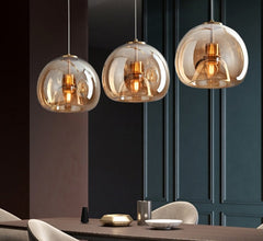 Three pendant ceiling lights with glass balls and metallic halide bulbs hang over a modern dining area with dark walls and light-colored furniture.