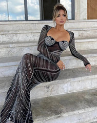 A woman sitting on steps wearing a long, black, glittery mesh full-sleeve dress with a square neckline and zippers.