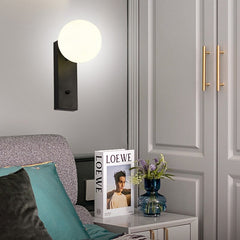 A  Frosted Glass Ball LED Metal Wall Sconce Light Fixtures in Black and white colours, over a side table beside a bed.
