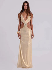 Woman wearing a gold halter cut-out maxi dress with beaded waist on a plain background.
