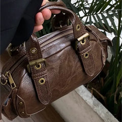 Retro coffee handbag with gold hardware and structured design held by a person, with a blurred background
