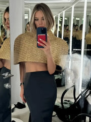 Mirror selfie wearing a gold sparkle cape-sleeve top with a high neck, styled with a fitted dark skirt in an indoor setting.