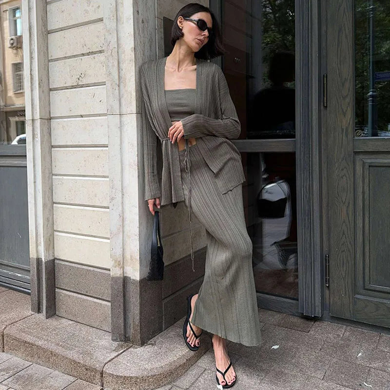 Woman in a gray knitted 3-piece sweater set—cardigan, lace-up top, and maxi skirt styled outdoors  standing outside a building