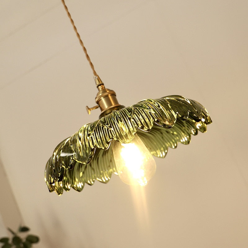 A hanging ceiling light with a green glass shade designed to resemble a flower, with a visible bulb and a metallic iron finish.