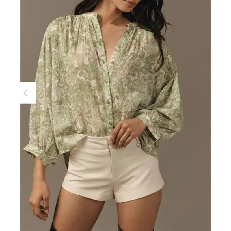 Woman wearing a green floral blouse and white shorts on a plain background