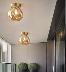 Two pendant ceiling lights with glass balls and metallic halide bulbs hang over a modern balcony area with dark walls and light-colored furniture.