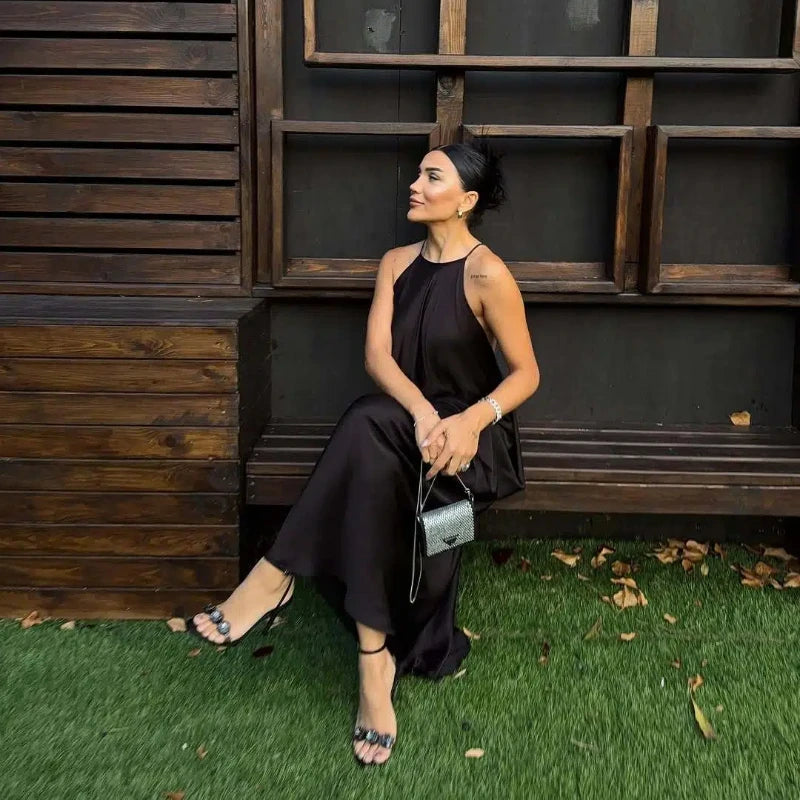 woman in a black halter backless maxi dress sitting on the bench