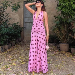 Woman wearing a pink polka dot dress standing outdoors with plants and a door in the background.