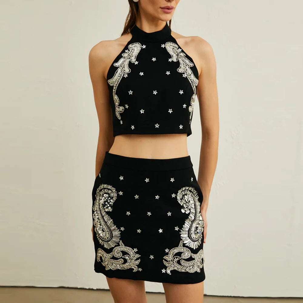 Model wearing a black halter top and high-waist mini skirt set with beaded detailing, posed against a neutral backdrop.