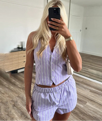 Close-up of a woman taking a mirror selfie wearing a matching single-breasted striped halter top detail outfit in a room.