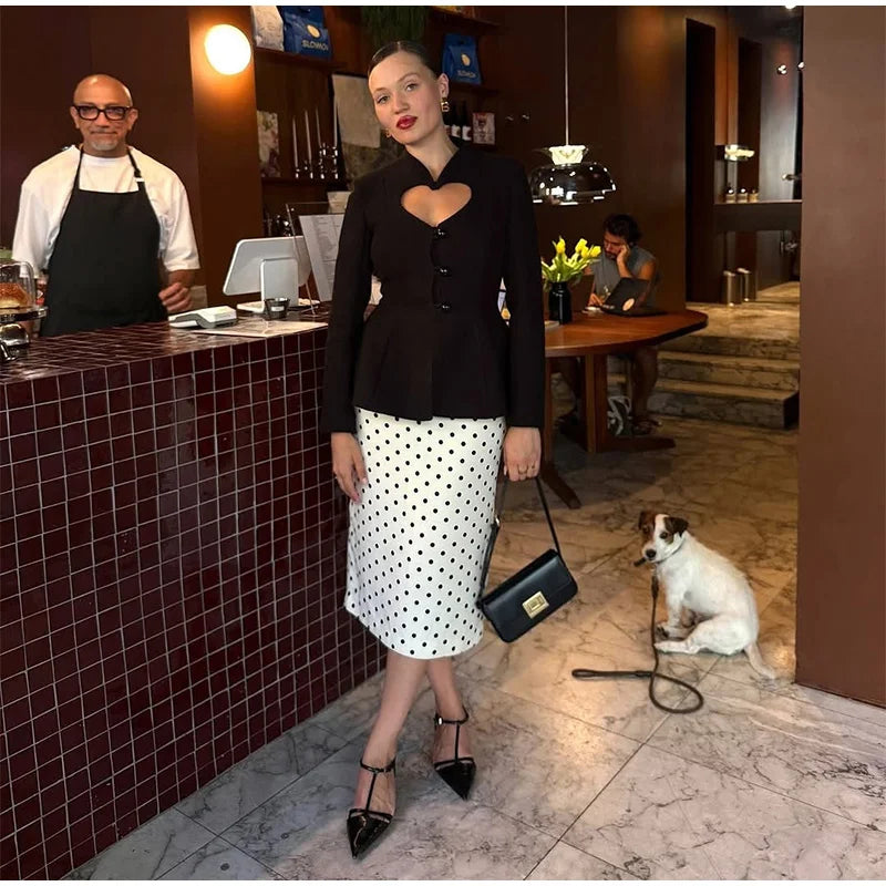 Street-style look featuring a black heart cutout blazer styled with a dotted skirt and slingback heels, creating a modern party-ready silhouette.