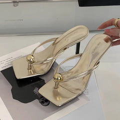 Gold high-heeled shoes with a gold ball design on a white surface.