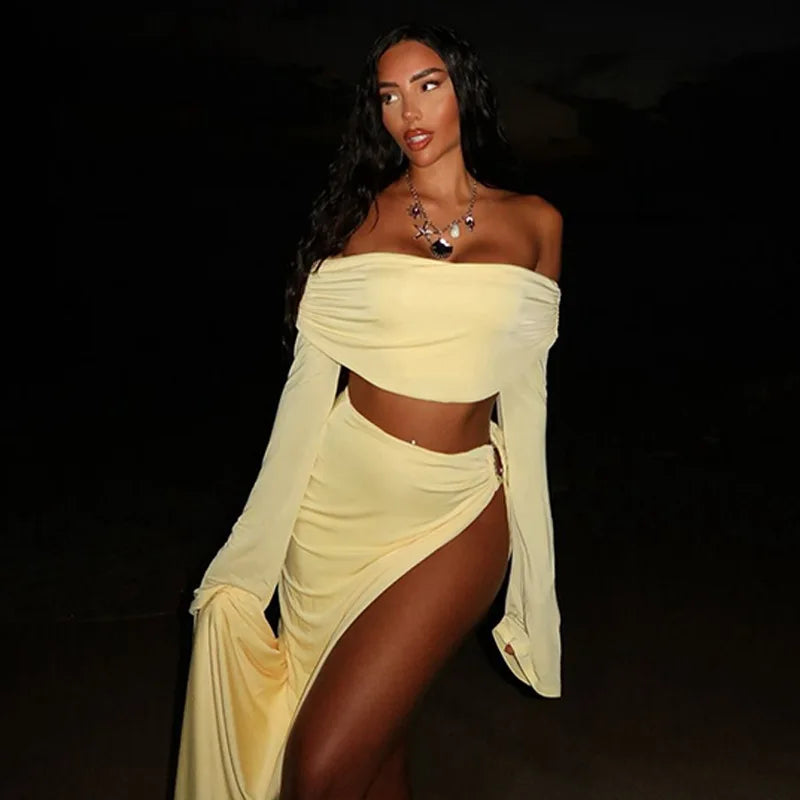 Woman wearing a high-slit ankle-length skirt with off-shoulder crop top against a dark background.