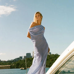 Woman in a  high street evening robe in blue mesh for upscale special occasions standing on a boat with a city skyline in the background