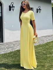 Woman in a high-waist ankle-length dress styled for warm weather, standing outdoors on grass with a white wall and black door in the background.