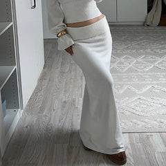 Person wearing a light-colored outfit with high waist slim long skirt with white pullover knit sweater worn by woman in a room with wooden flooring.
