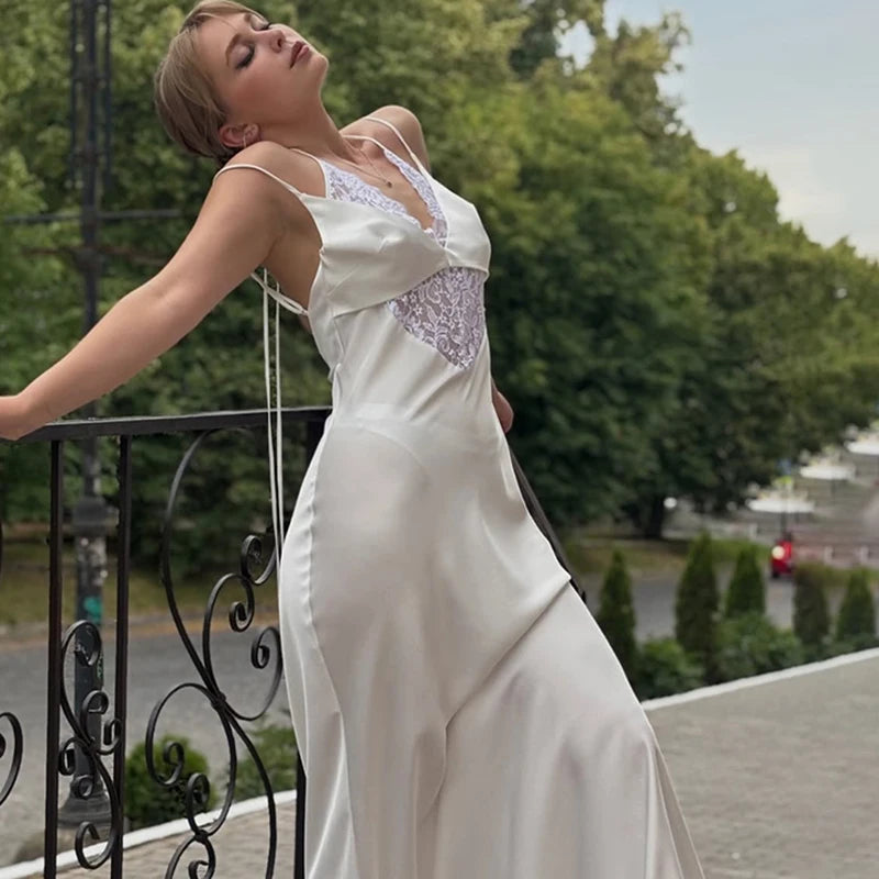 Woman in a hollow out sleeveless party dress in white for summer special occasions standing on a balcony with greenery in the background