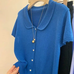 Blue cardigan with a necklace on a hanger against a neutral background