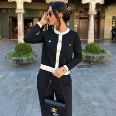 Woman in a INS hot fashion 2025 knitted top for juniors in contrast color-block standing in an outdoor setting with columns and plants.