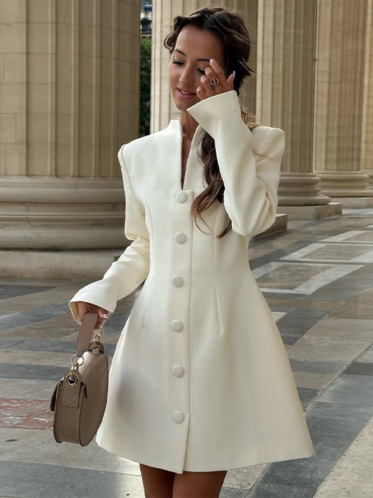 Woman wearing an ivory high-neck button-front mini dress, photographed outdoors in front of classical columns with a structured handbag.