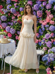 Woman in an ivory strapless long dress standing before a colorful flower wall, showing a draped bodice and airy A-line skirt.