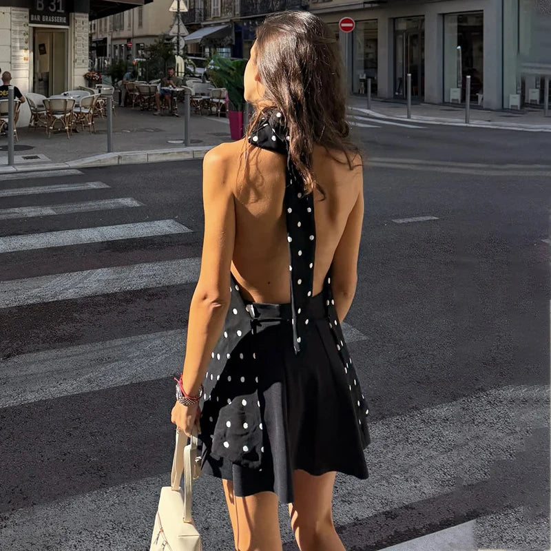 Woman in a  junior party casual polka dot halter blouse black for summer club looks dress crossing a street in an urban setting.