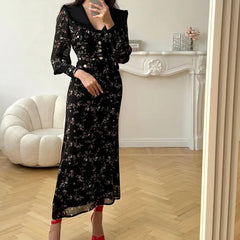 Person wearing a long-sleeved, ankle-length, A-line slim fit dress with metal buttons in a room with a white armchair and decorative items.