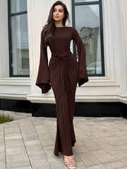 Woman wearing a brown dress with bell sleeves standing outside a building.