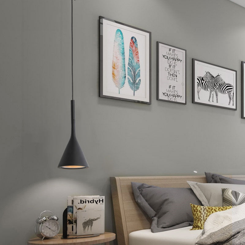 A pendant LED ceiling light fixture with a black metal finish hangs in a bedroom setting with decorative artwork on the walls.