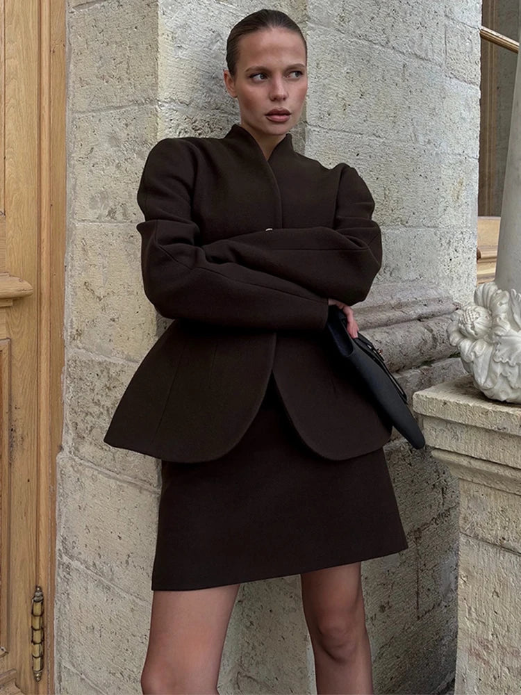 Street-style look of a deep brown two-piece jacket and mini skirt set, styled for cool-weather city dressing with a refined silhouette.