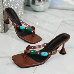 Brown high-heeled sandals with turquoise stones on a reflective surface