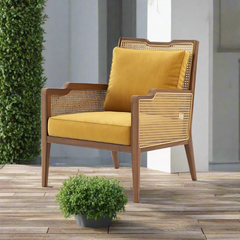 A modern leisure rattan wicker arm dining chair with a yellow cushion, situated on a wooden floor with a potted plant beside it.
