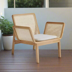 A natural rattan wicker chair with a solid teak wood frame and a white cushion backrest, standing on a wooden deck.